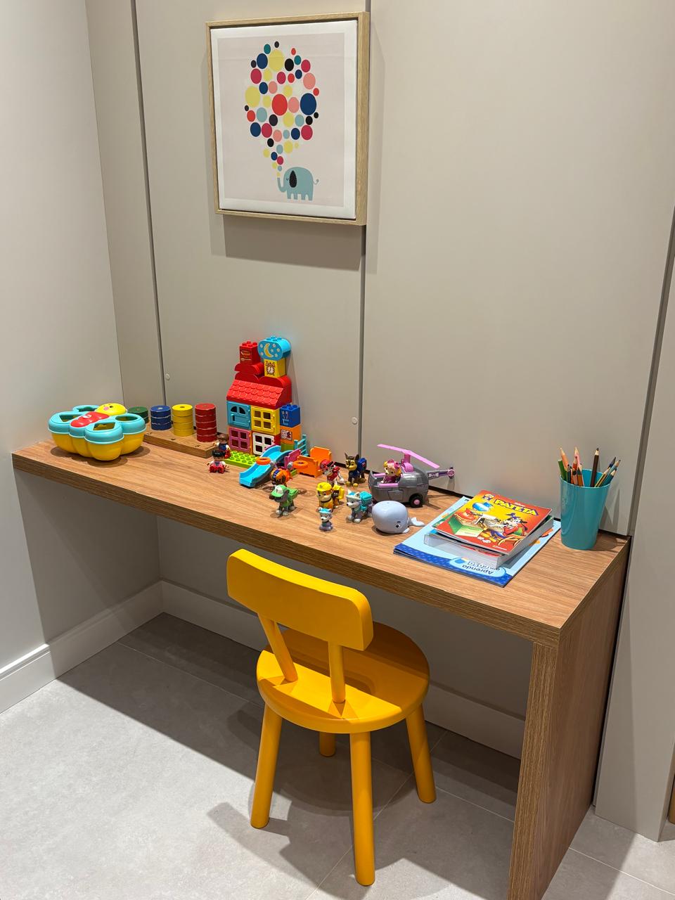 Espaço kids com mesinha, cadeira amarela, brinquedos e livros